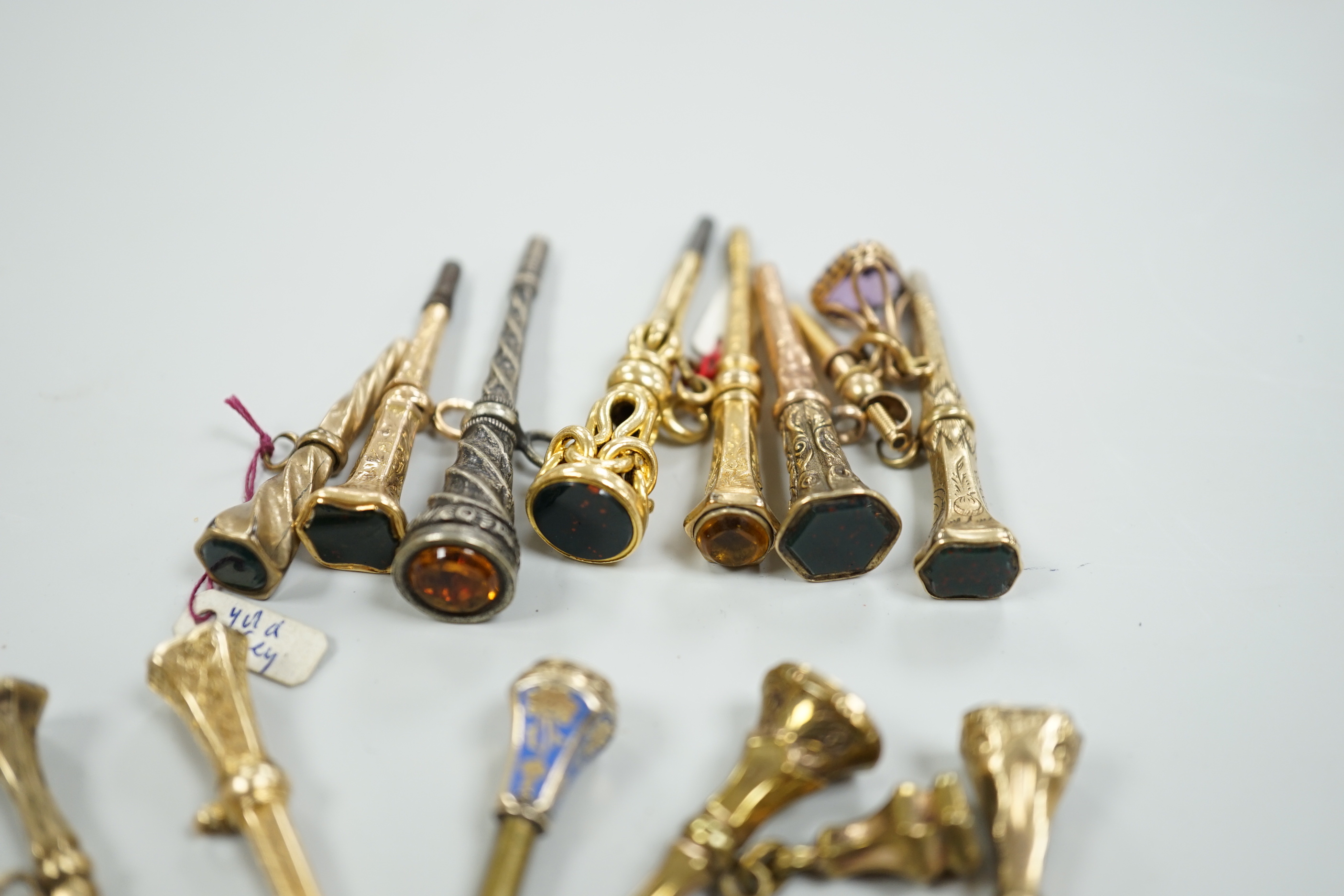 Fifteen assorted 19th century mainly yellow metal overlaid and gem set watch keys, including bloodstone, citrine and white chalcedony and one with enamel, mostly of trumpet form, largest 51mm.